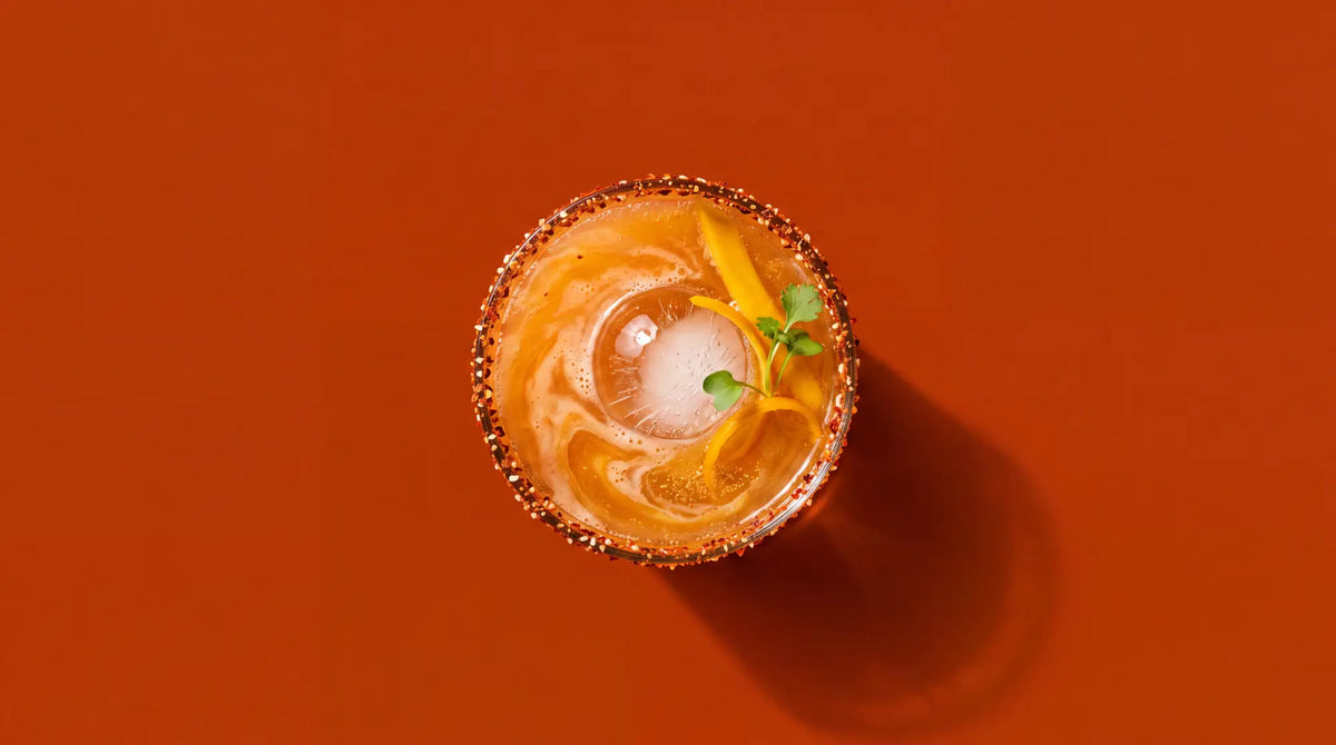 A vibrant orange ginger lime far east margarita fizz cocktail in a salt-rimmed glass with citrus twist and fresh herbs