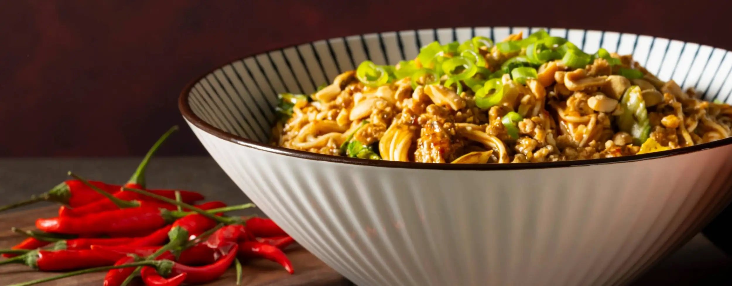A white ceramic bowl with black striped rim and ridges filled with stir-fried noodles topped with green onions for hanoi dandan noodle recipe