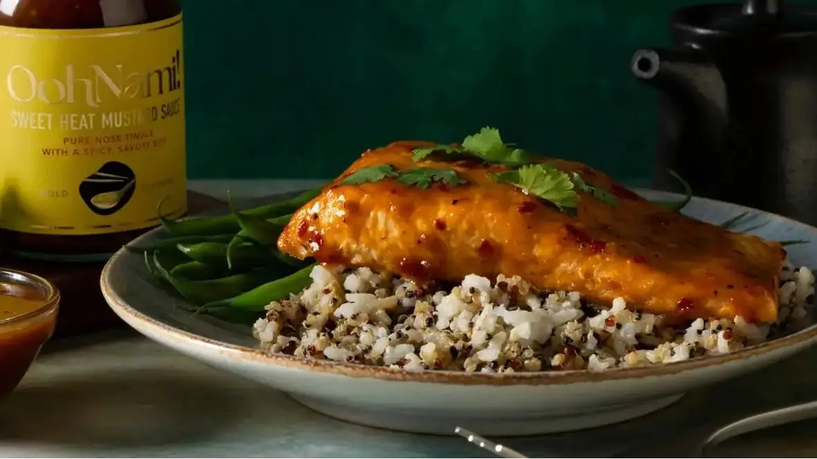 A golden brown sweet chili mustard baked salmon fillet on mixed quinoa and green beans garnished with fresh cilantro