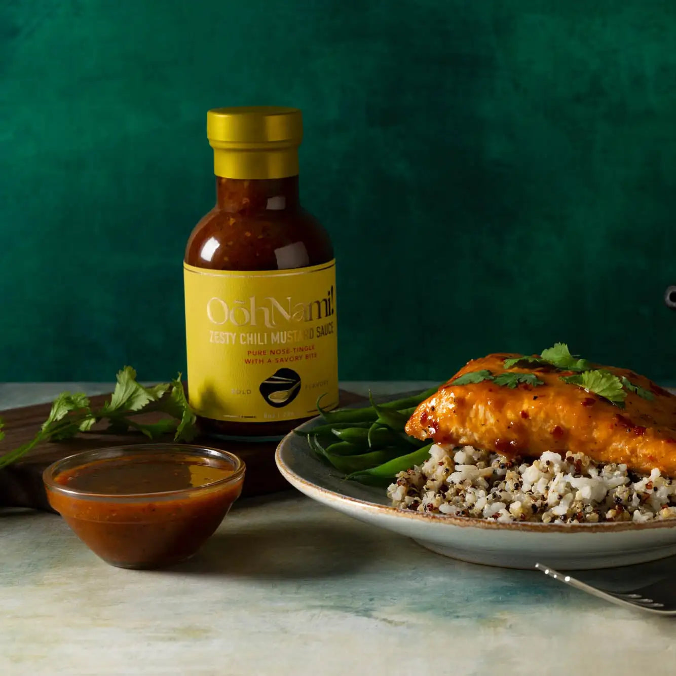 A bottle of ooh nam! Spicy chili mustard sauce with a yellow label and gold cap, filled with a rich brown condiment.