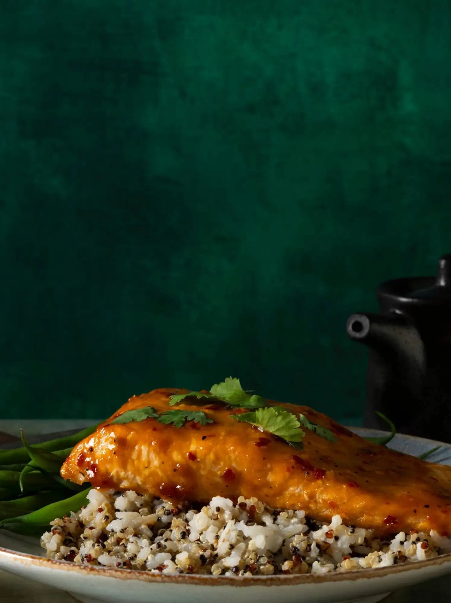 A golden glazed salmon fillet rests atop a bed of mixed quinoa and green beans, garnished with fresh cilantro.