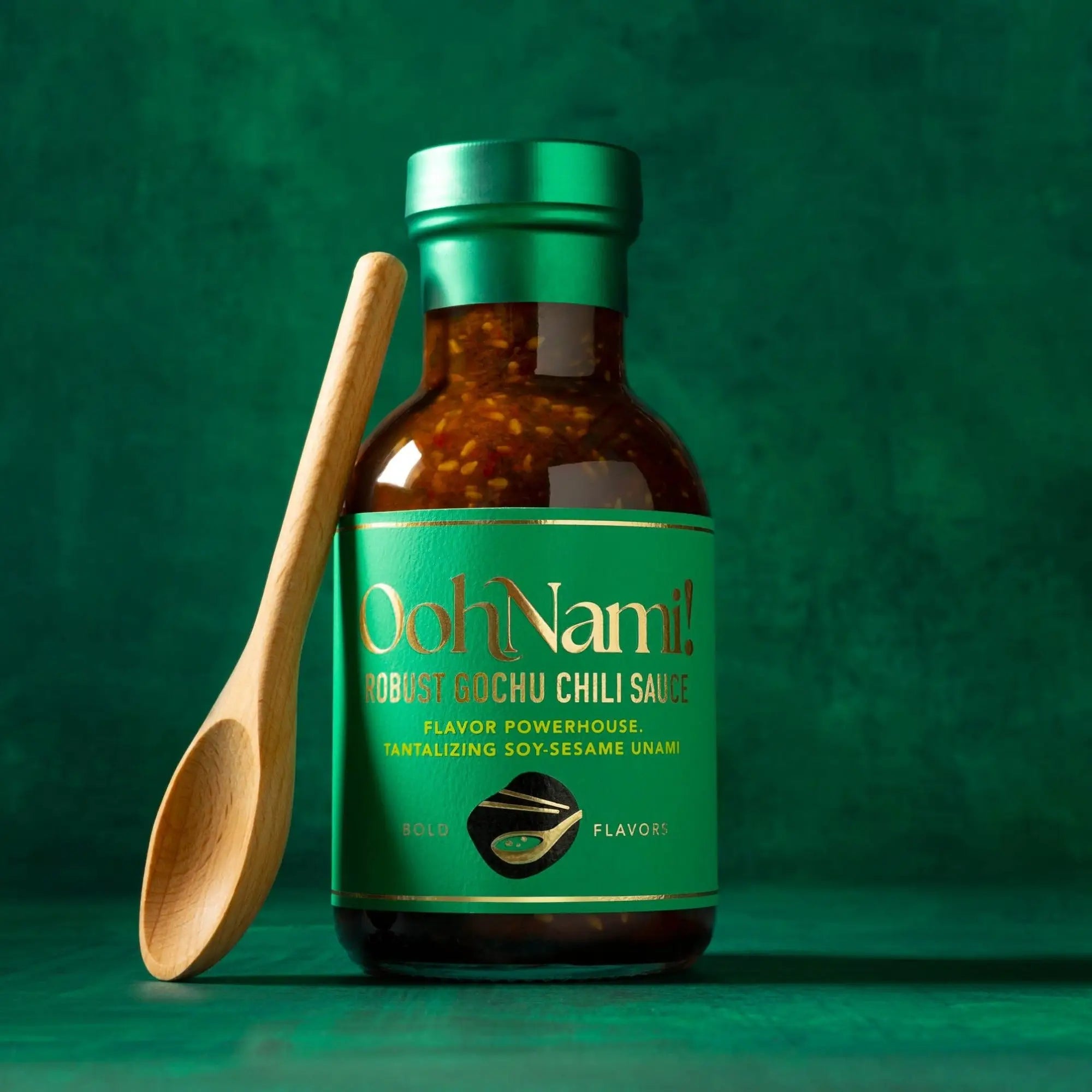 A bottle of ooh nami robust gochu chili sauce with a green label and metallic cap filled with brown sauce and chili flakes