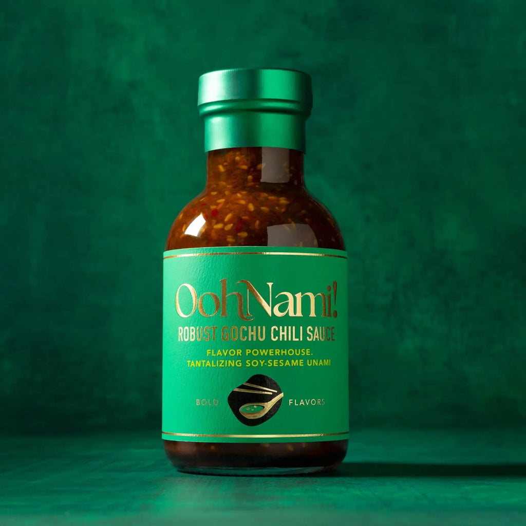 A bottle of oohnami robust gochu chili sauce with a green label and metallic cap filled with red chili sauce