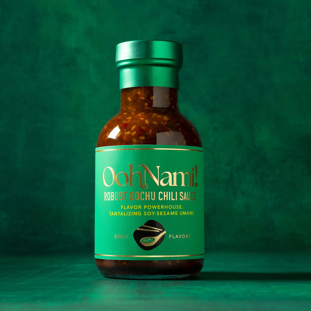 A sleek glass bottle of oohnami robust gochu chili sauce with a green label filled with rich red chili sauce and sesame seeds