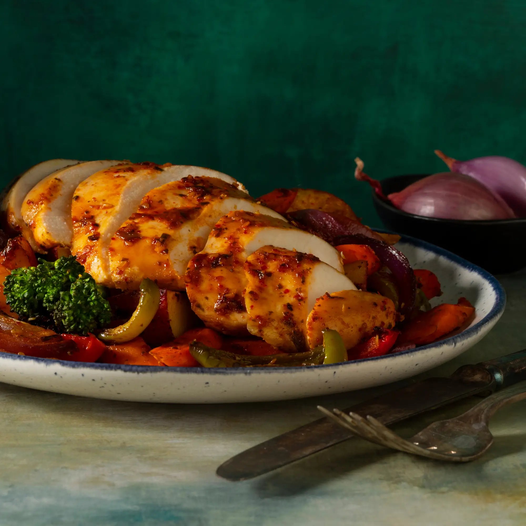 Sliced grilled chicken breast with golden spice coating served on roasted vegetables on a plate for robust gochu chili sauce