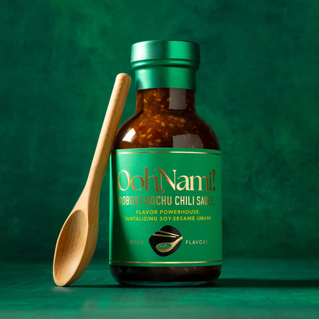 A vibrant green glass bottle of oohnami robust sochu chili sauce with chili flakes in rich amber sauce and gold lettering