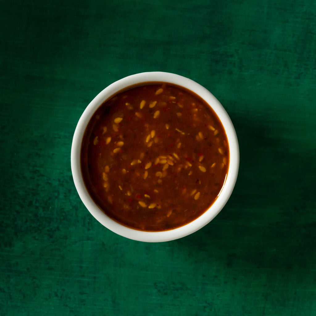 A white ceramic bowl with robust gochu chili sauce in reddish-brown color speckled with golden sesame seeds