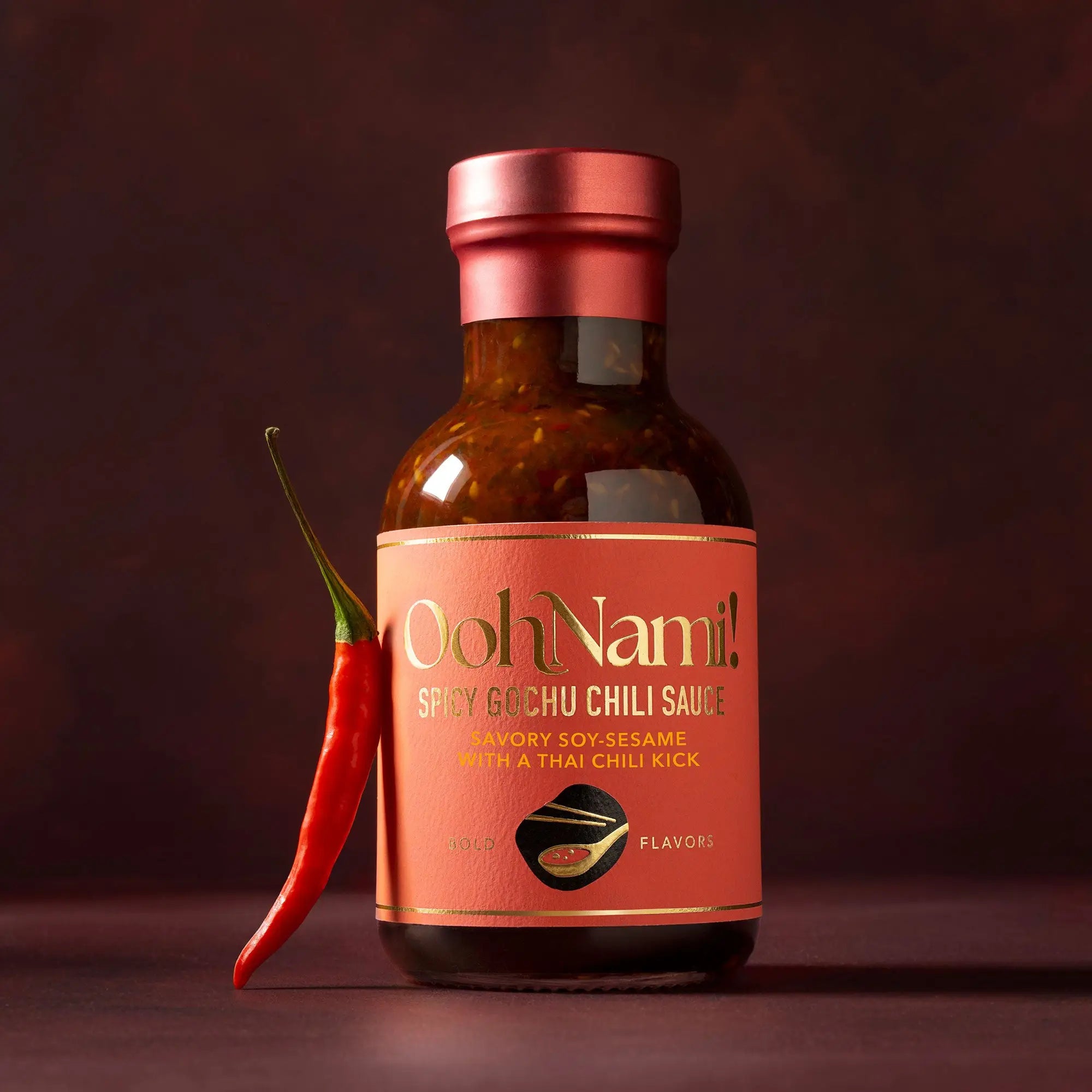 A bottle of ooh nami spicy gochu chili sauce with vibrant orange label and rose gold cap featuring soy sesame flavor