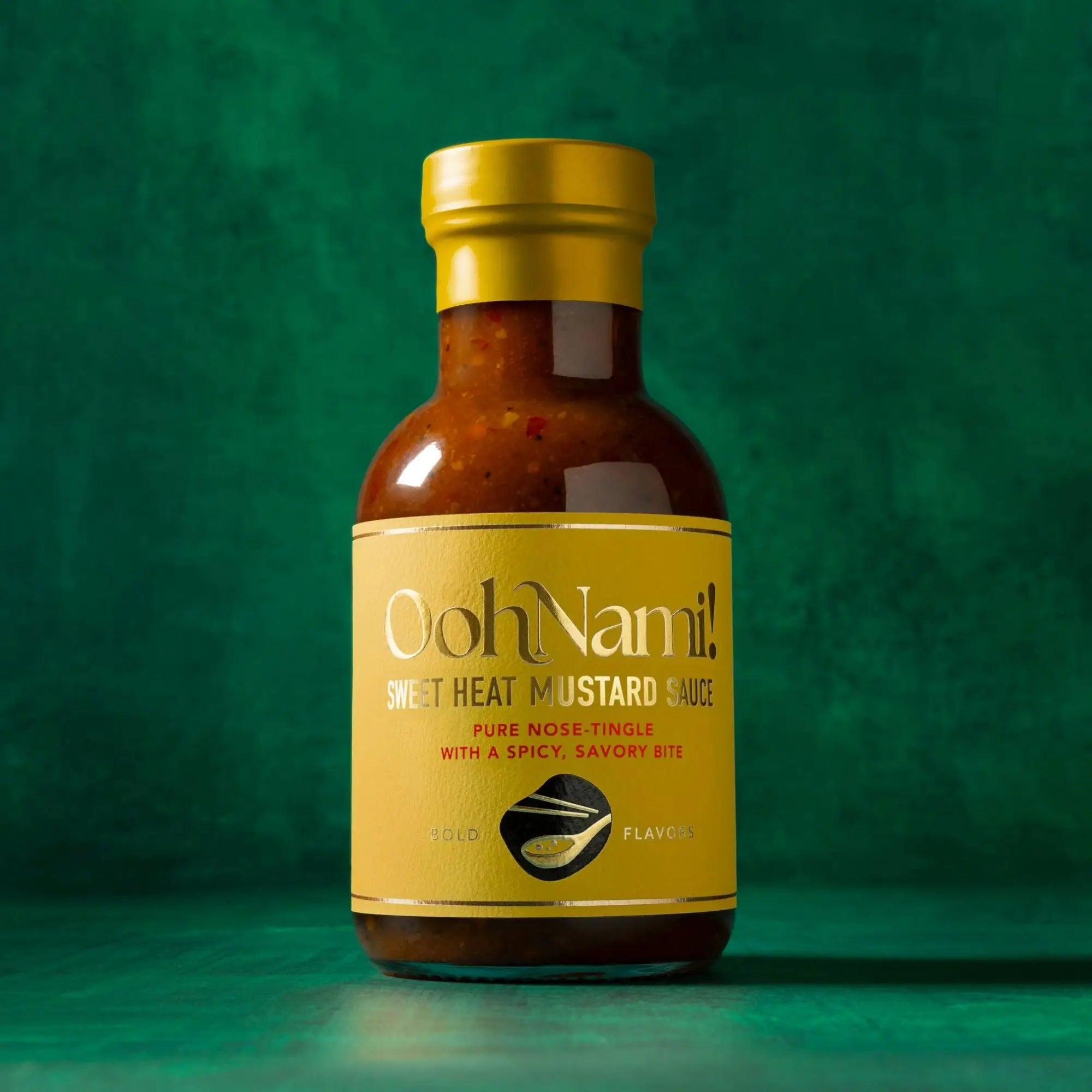 A bottle of oohnami sweet heat mustard sauce with a golden cap and vibrant orange-red sauce inside