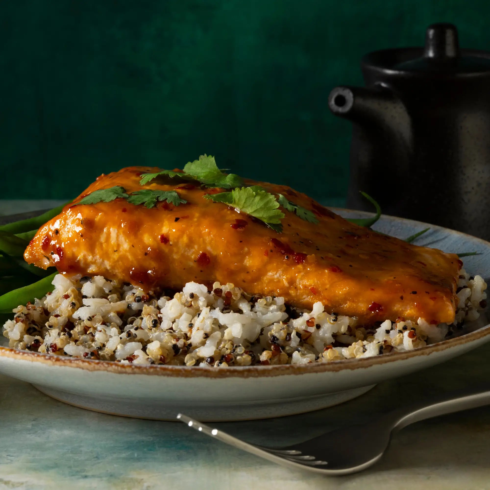 A golden glazed salmon fillet on multigrain quinoa and green beans garnished with cilantro served with sweet heat mustard sauce