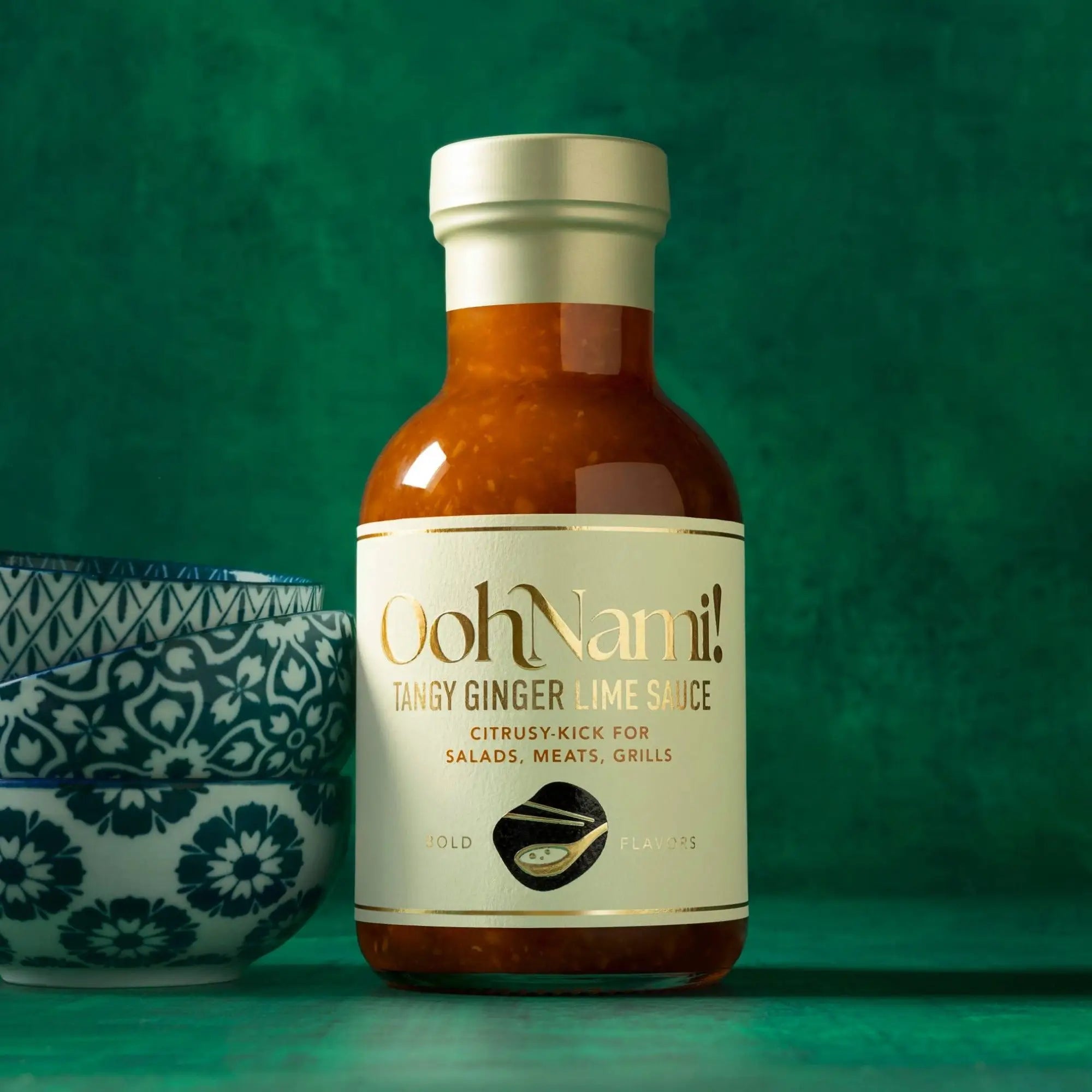 A sleek glass bottle of oohnami tangy ginger lime sauce with amber-orange sauce and metallic silver cap