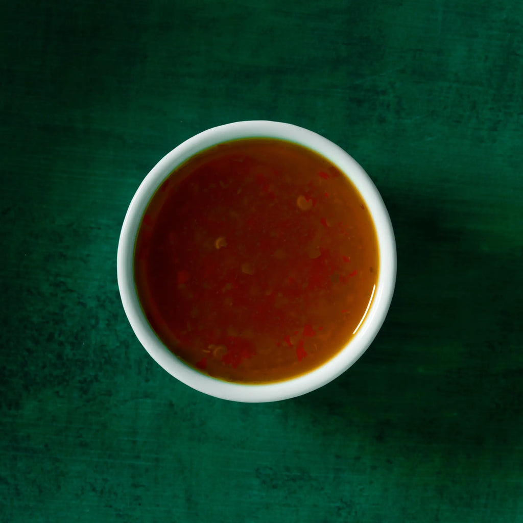 White ceramic bowl filled with glossy reddish brown tangy ginger lime sauce with visible red flecks