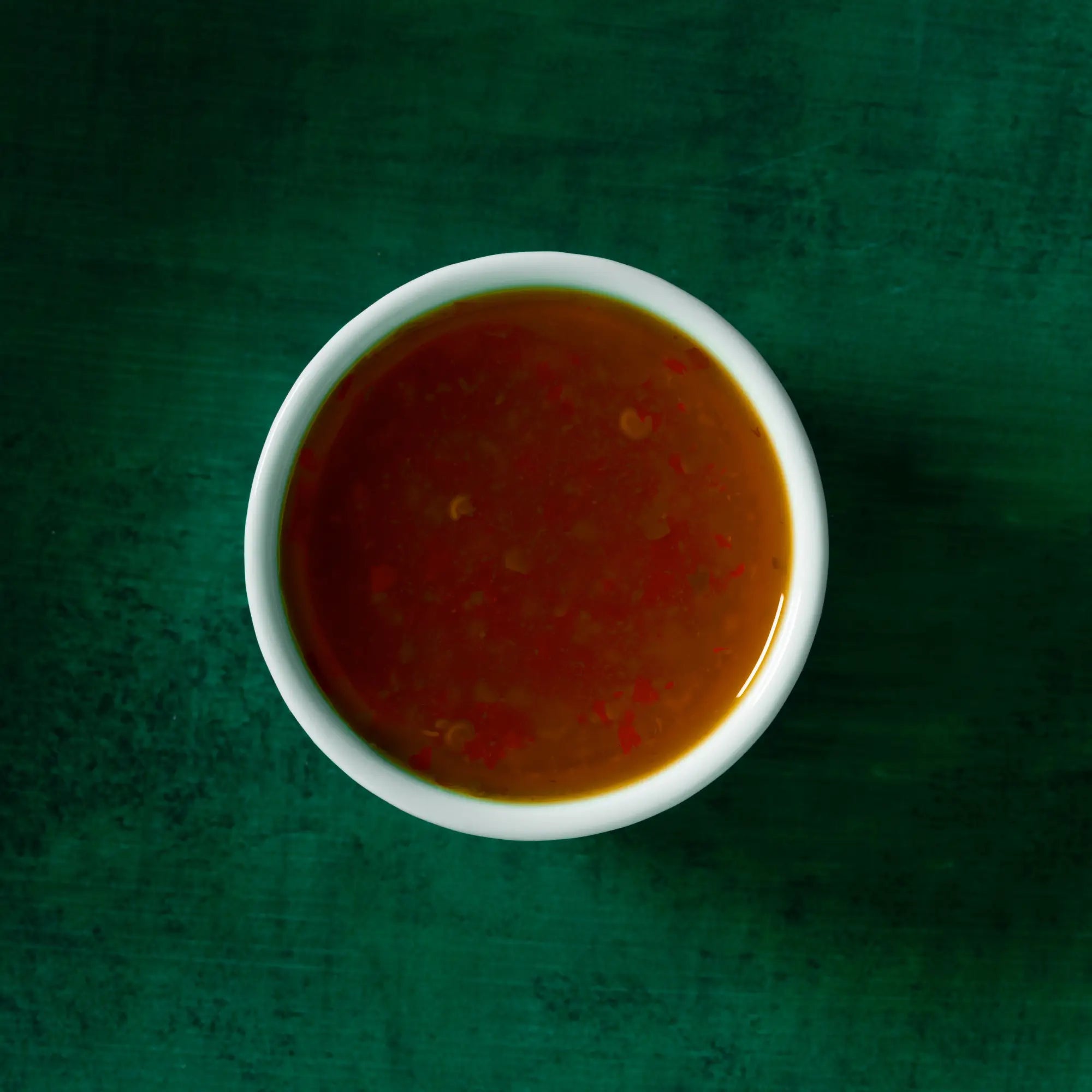 White ceramic bowl filled with glossy reddish brown tangy ginger lime sauce with visible red flecks