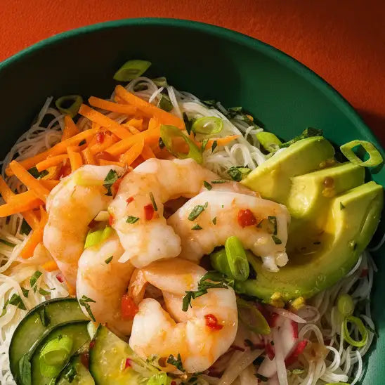 A vibrant green bowl filled with a colorful salad of shrimp, avocado slices, shredded carrots, and noodles.