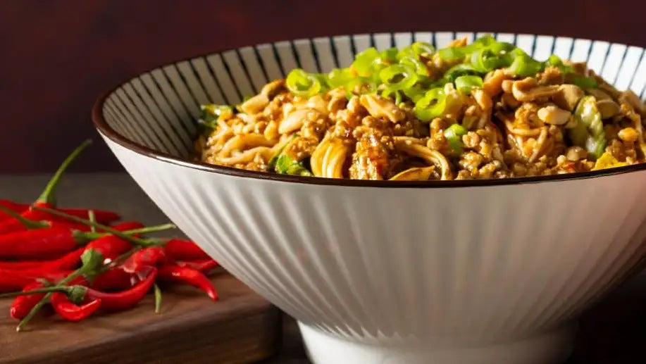 A white ceramic bowl with a black rim and vertical striped pattern, filled with a savory noodle dish topped with chopped green onions.