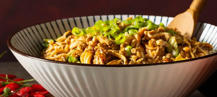 A white ceramic bowl with black vertical stripes and a fluted rim, filled with stir-fried noodles topped with chopped green onions.