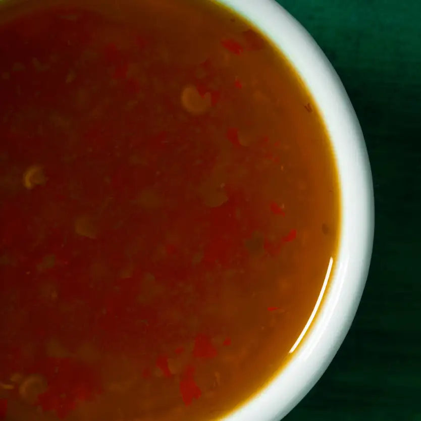 A white ceramic bowl filled with a rich, amber-colored sauce speckled with red chili flakes.