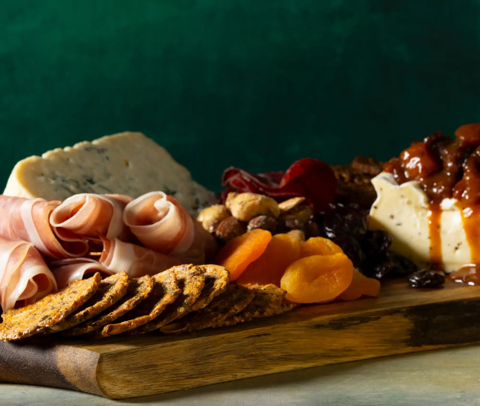 Wooden cutting board with assorted cheeses, cured meats, dried fruits, nuts, and crackers arranged on its surface.